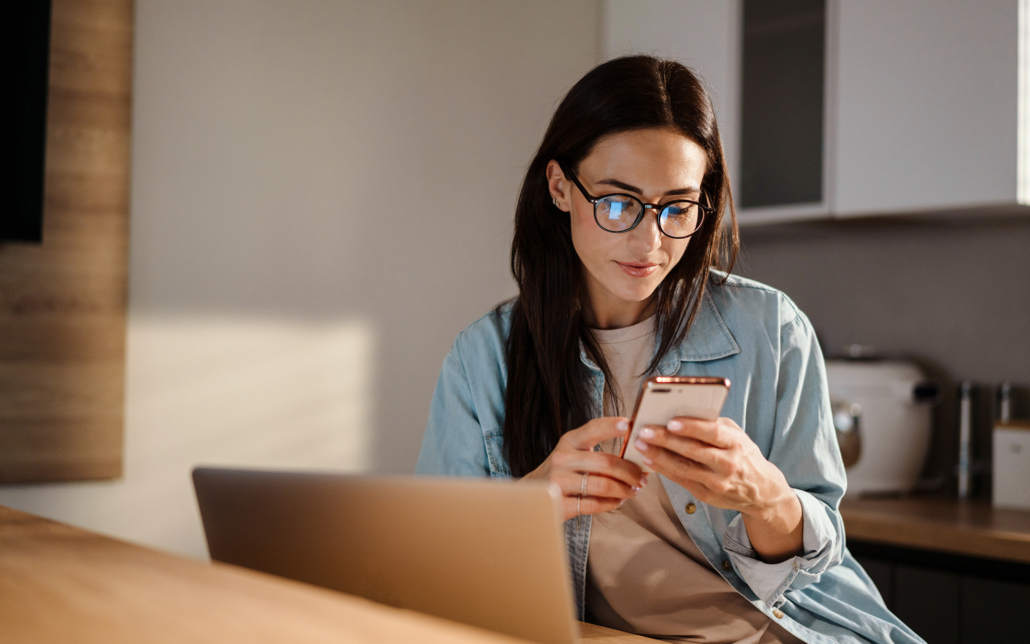 Serious Charming Woman Using Smartphone While Working With Laptop