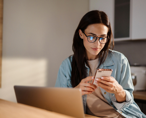 Serious Charming Woman Using Smartphone While Working With Laptop