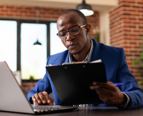 Entrepreneur Working With Laptop And Files On Clipboard To Plan